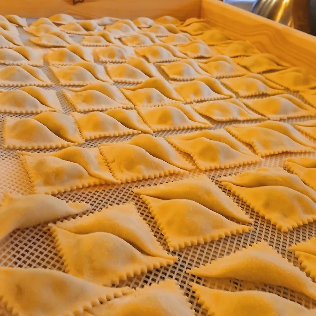 Pasta fresca ripiena dai bordi dentellati in file ordinate su una griglia per essiccare in un vassoio di legno, preparata da Buò